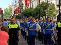 Desfile militar en una calle de la ciudad, con soldados en uniforme y banderas ondeando en el fondo.
