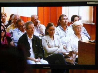 Una sala de audiencias con personas sentadas en bancas, algunas sonriendo.