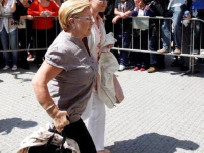 Una mujer con una camisa gris y pantalones negros, sosteniendo un bebé en brazos mientras camina entre una multitud de personas. La imagen muestra a la mujer con un vestido blanco y pantalones blancos, caminando entre una multitud de personas. La imagen muestra a la mujer con un vestido blanco y pantalones blancos, caminando entre una multitud de personas.