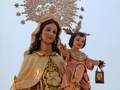 Estatua religiosa de una mujer con un niño en sus brazos, vestida con trajes ornamentados y una corona estrellada. La imagen destaca la importancia de la devoción religiosa y el culto a las santas.