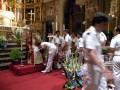 Una procesión religiosa en una iglesia con sacerdotes vestidos de blanco y un altar adornado.