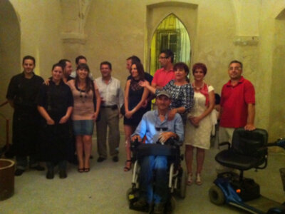 Una familia multigeneracional posa en una sala con arcos, incluyendo un hombre en silla de ruedas y una mujer en silla de ruedas.