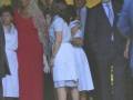Una mujer vestida con un vestido rojo largo y una falda de encaje, junto a otros personajes formando parte de un evento formal.