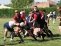 Un equipo de rugby en acción, jugando un partido en un campo verde. Los jugadores están concentrados y luchan por controlar el balón, con una escuela en el fondo.