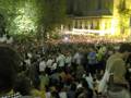 Una multitud en un concierto nocturno frente a una iglesia iluminada.