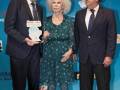 Premios Solidaridad, Festival de las Naciones. Mujer con vestido verde y zapatos azules recibe un premio junto a dos hombres en trajes.