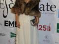 Elegante mujer en vestido blanco con capa de piel, posando en un evento de gala.