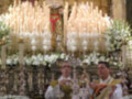 Imagen de dos personas vestidas con trajes ceremoniales, posiblemente sacerdotes, frente a un altar adornado con flores y velas encendidas.