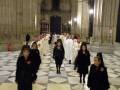 Una procesión religiosa en una catedral, con sacerdotes vestidos de blanco y monjas negras caminando en fila.