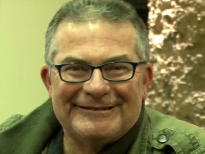 Retrato de hombre sonriente con gafas y chaqueta verde, fondo sutilmente texturizado.
