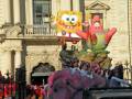 Un desfile navideño con un globo de Bob Esponja y un personaje rojo en el centro, frente a una fachada de estilo colonial.