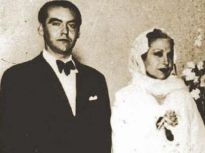 Dos personas posan en una imagen antigua, uno con traje formal y la otra con vestido blanco y velo.