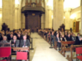 Interior de una catedral con un gran grupo de personas sentadas en bancos, escuchando una ceremonia o discurso formal.