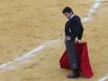 Un torero en el centro de la plaza de toros, con su capote rojo y su traje tradicional, preparándose para la corrida de toros.