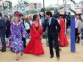 Una escena festiva con jóvenes vestidos de flamenca en color rojo y azul, caminando por un camino arenoso con decoración navideña.