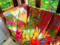 Colorful, patterned fabric draped over a wooden chair, illuminated by natural light from a window with a view of greenery.