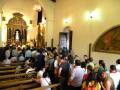 Interior de una iglesia con personas reunidas, destacando el altar y la decoración arquitectónica.
