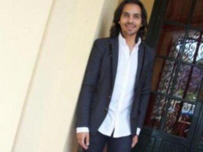 Hombre con traje y camisa blanca, sonriendo en un entorno urbano.