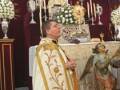 Un sacerdote en traje sacerdotal celebra una misa en un altar adornado con flores y una imagen de la Virgen María.