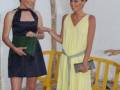 Dos mujeres posan con vestidos de fiesta, una en azul y otra en amarillo. Ambas llevan clutch y su postura sugiere una celebración o evento formal.