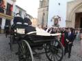 Una imagen de una ceremonia en un entorno histórico, con personas vestidas formalmente y un carro antiguo.