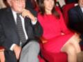 Una mujer en un vestido rojo asiste a una conferencia de prensa, sentada entre hombres en trajes.