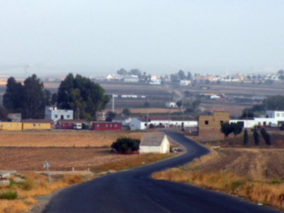 Vista de una carretera que se extiende hacia una ciudad con edificios y campos agrícolas en el horizonte.
