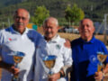 Tres hombres celebran con trofeos en un evento al aire libre, rodeados de naturaleza.