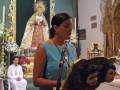 Mujer en traje azul hablando en un micrófono en una iglesia con el altar y la Virgen de Guadalupe en el fondo.