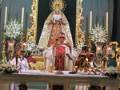 Elegante altar con una imagen de la Virgen María y un crucifijo en el centro, rodeado de velas y flores, en un ambiente festivo y religioso.