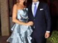 Una mujer con un vestido blanco y negro con detalles metálicos, posa junto a una persona en traje azul. Ambos parecen estar en un evento formal, posiblemente una boda o cena de gala.