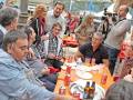 Un grupo de personas disfrutando en un restaurante al aire libre, con mesas llenas de bebidas y comidas. La atmósfera es animada, con gente conversando y tomándose fotos.