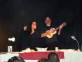 Músico tocando la guitarra y cantante en un escenario con público en primer plano.