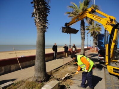 Trabajadores realizando tareas de mantenimiento en un paseo marítimo junto a la playa.