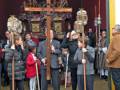 Una procesión religiosa en un ambiente festivo, con personas vestidas de manera formal y portando cruces y antorchas.