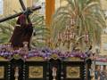 Estatua de Jesús con la cruz en una procesión religiosa, rodeada de flores y decoraciones.