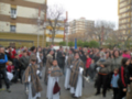 Una multitud de personas participa en una procesión religiosa, con vestimentas tradicionales y máscaras. La imagen muestra un ambiente festivo en una calle con edificios al fondo, probablemente durante una celebración cultural o religiosa importante.