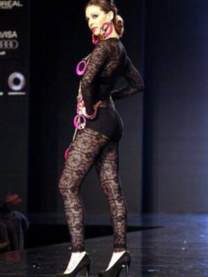 Una modelo con un vestido negro de encaje y accesorios brillantes camina por la pasarela.