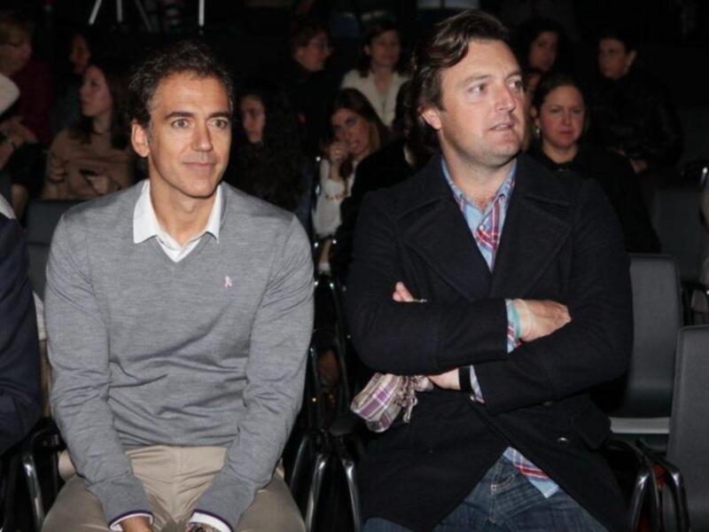 Dos hombres asisten a un evento en un auditorio lleno de personas.