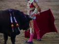 Un torero en traje tradicional se prepara para enfrentarse a un toro negro en una plaza de toros.