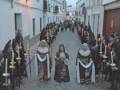 Procesión histórica con vestimentas tradicionales y velas en una calle adoquinada.