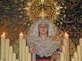 Estatua de Virgen María con vestimentas tradicionales y una corona de oro, rodeada de velas en un ambiente de iglesia con detalles dorados en el techo.