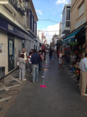 Calle peatonal con tiendas y gente caminando bajo un cielo azul.