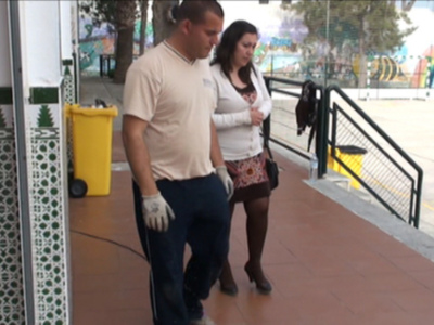 Dos personas caminan por una calle, uno con guantes y la otra con un bolso. Al fondo se ve una parada de autobús con grafitis y una gran arcoíris.