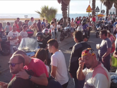 Una multitud de personas reunidas en una calle con motocicletas y palmeras, disfrutando de un evento al aire libre.