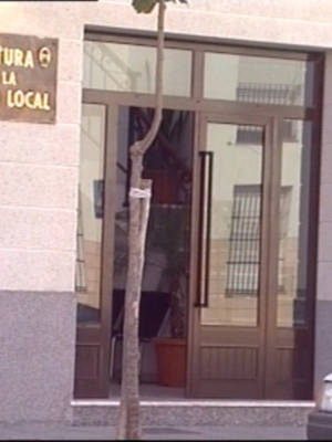 "JEFATURA DE LA POLICÍA LOCAL. Sede de la Policía Local en una estructura con puerta principal y un coche estacionado a su lado. La imagen muestra una entrada formal con detalles arquitectónicos."