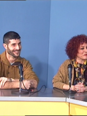 Dos personas sentadas en una mesa con micrófonos, posiblemente en una conferencia o entrevista.