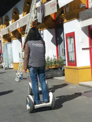 Persona montada en una scooter eléctrica en una calle con edificios históricos y comercios locales.