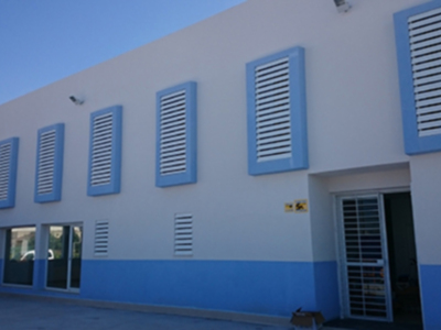 Fachada de un edificio moderno con ventanas azules y blancas, iluminación exterior y una puerta principal.