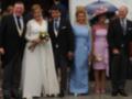 Boda en un ambiente formal, con una novia en un vestido blanco, un novio en traje negro, y dos damas de honor en vestidos de color azul y rosa.